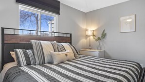 Una camera da letto con un letto, un comodino con una lampada, una finestra con persiane e una ventola a soffitto.