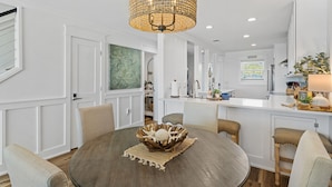 Une cuisine moderne avec des meubles blancs, un îlot central doté de tabourets et un lustre décoratif.