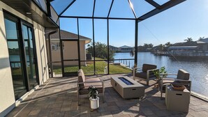 A covered patio with outdoor furniture, a fire pit, and a view of a body of water. - New home on Gulf access water near beaches! (Cape Coral)