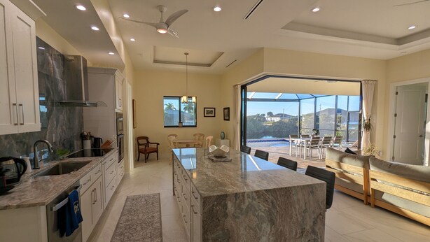 A modern kitchen with a large island, built-in appliances, and a view of a pool and landscape. - New home on Gulf access water near beaches! (Cape Coral)