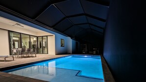 An indoor swimming pool with a tiled deck, a ceiling fan, and a glass door leading to a room with a dining area. - New home on Gulf access water near beaches! (Cape Coral)