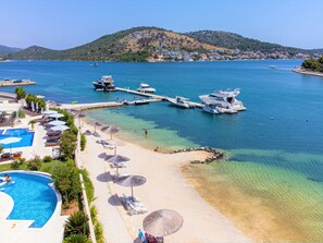 Enjoy a beachside retreat with a swimming pool, sun loungers, and umbrellas for shade, adjacent to a dock with opportunities for water activities.