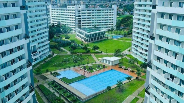 Ett högt bostadshuskomplex med flera våningar, en central innergård med en swimmingpool och omgivande grönska.