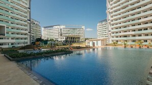 En swimmingpool omgiven av moderna byggnader med balkonger, en lekplats och en klar himmel.