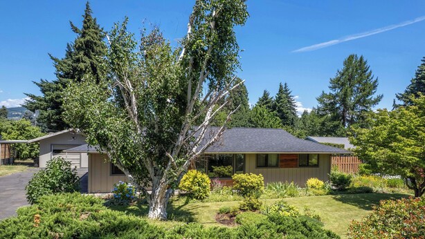 A single-story house with a garage, surrounded by a well-maintained garden and tall trees.