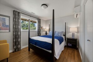 A bedroom with a four-poster bed, a bedside table with a lamp, a chair, and a window with curtains. - Belle of the Ball! Biking, Wineries, Westside Hood River! (Hood River)