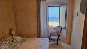 A hotel room with a bed, a chair, a window with a view of the beach, and a door. - Casa Torra d'Erbalunga (Cateri)