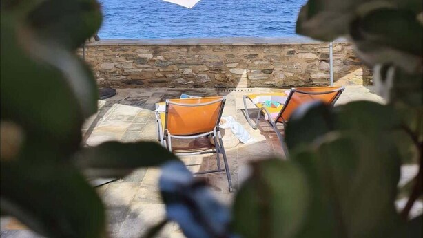 A stone wall with a view of the sea, two orange chairs, and a table under a large umbrella. - Casa Torra d'Erbalunga (Cateri)