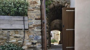 A stone courtyard with a wooden door leading to an archway, surrounded by stone walls and a wooden bench. - Casa Torra d'Erbalunga (Cateri)