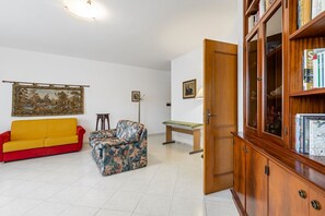 Un salon avec un canapé rouge, un fauteuil à motifs, un meuble en bois rempli de livres et un tableau accroché au mur.