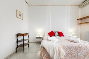 Une chambre à coucher comprenant un lit, des tables de chevet, une petite table et une étagère fixée au mur.