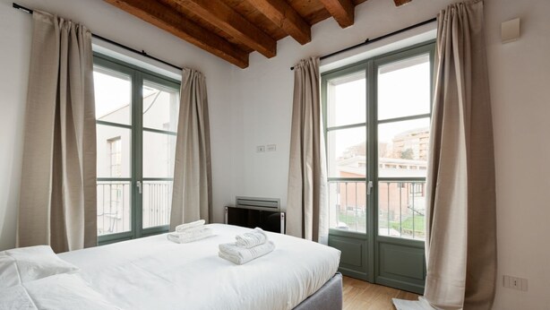 Un dormitorio con cama, cortinas, radiador y ventana con vistas.