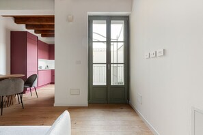 Un interno moderno con pavimento in legno, zona pranzo con tavolo e sedie, cucina con mobili rosa e una porta verde.