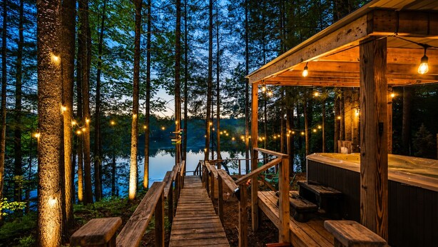 Eine Holzterrasse führt zu einer Hütte mit Whirlpool und Lichterketten.