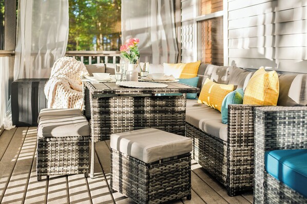 A wicker sofa set with cushions, a small table with a vase of flowers, and a bench.