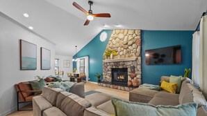 Ein modernes Wohnzimmer mit Kamin aus Stein, Deckenventilator und großem Fernseher an der Wand.