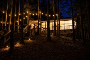 A wooden cabin with a staircase, surrounded by trees, and string lights.