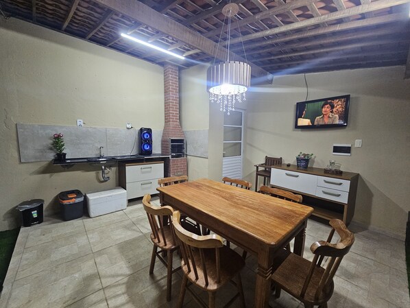 A dining area with a wooden table and chairs, a brick chimney, and a television mounted on the wall.