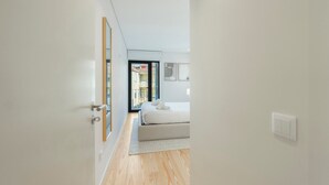 Un pasillo estrecho que conduce a un dormitorio con una cama, un espejo grande y vistas al exterior.