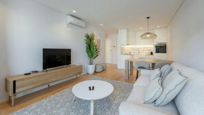 Una sala moderna con un televisor de pantalla plana, un mueble bajo de madera, una mesa de centro blanca y un sofá gris.