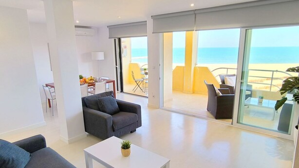 A modern living room with a sofa, a coffee table, and a balcony with a view of the beach.