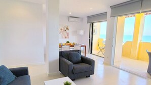A modern living room with a sofa, a coffee table, and a dining area in the background.