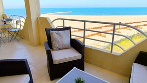 A balcony with wicker furniture, a view of the beach, and a clear sky.