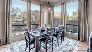 A dining area with a table set for four, large windows with curtains, and a hanging light fixture. - Experience luxury at Sedona Birdsong, a 3-bed retreat in Village of Oak Creek. (Sedona)