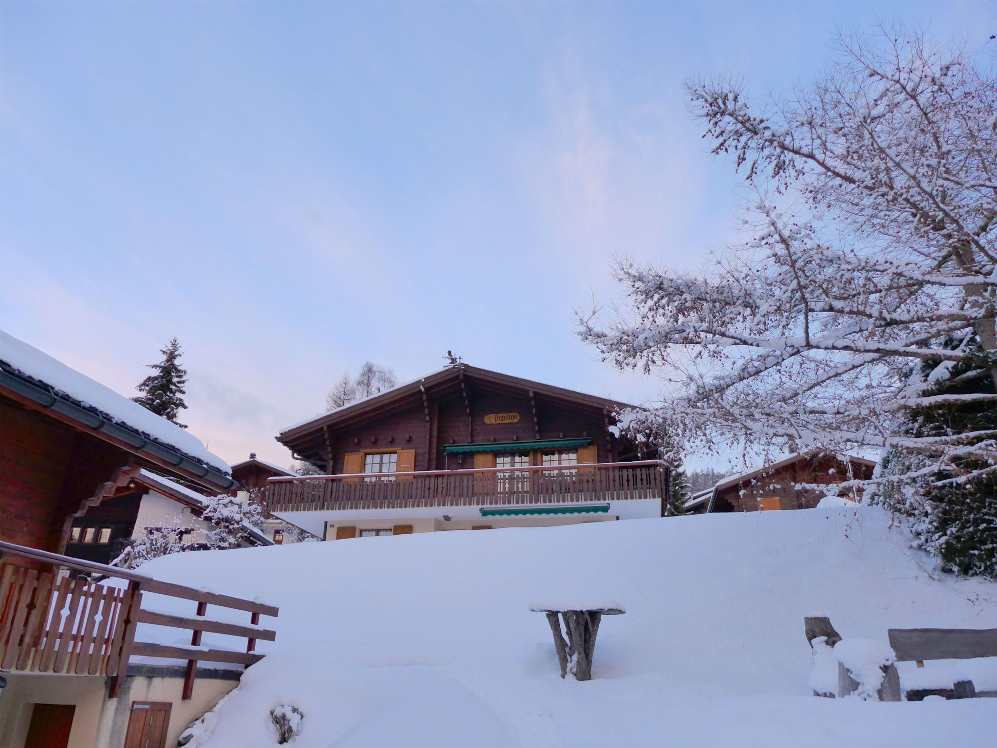A snow-covered lodge with a balcony and a wooden fence.