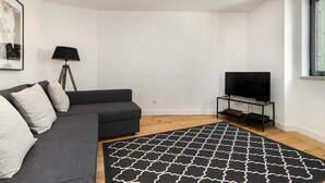 Una sala de estar moderna con un sofá gris, una lámpara de pie negra, un tapete con estampado blanco y negro y un televisor sobre un pedestal negro.