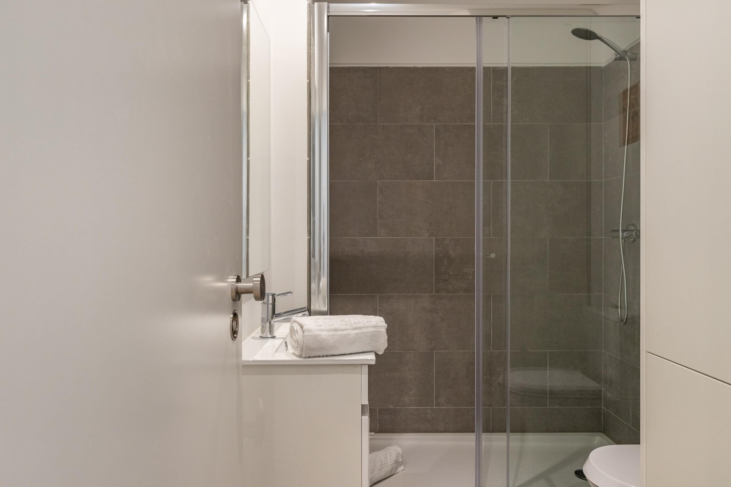 Een moderne badkamer met een douchecabine van glas, een witte wastafel en een handdoek op het aanrecht.