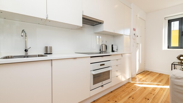 A modern kitchen with white cabinets, stainless steel appliances, and a wooden floor.
