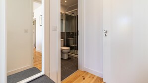 A narrow hallway leading to a bathroom with a toilet, shower, and a glass-enclosed shower area.