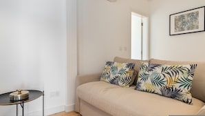 A minimalist living room with a beige sofa, two patterned pillows, a small round table with a decorative item, and a wall-mounted air conditioner.