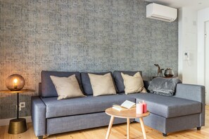 Una sala de estar moderna con un sofá gris, una mesa de centro redonda de madera y un papel tapiz estampado.
