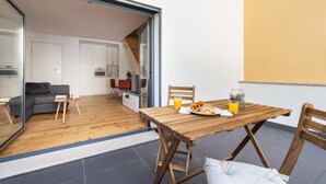 Un espacio habitable moderno con una mesa de madera preparada para el desayuno, un sofá y una cocina visible a través de una puerta abierta.