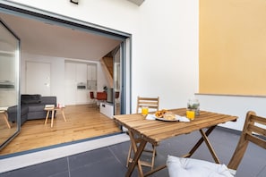 Un espacio habitable moderno con una mesa de madera preparada para el desayuno, un sofá y una cocina visible a través de una puerta abierta.