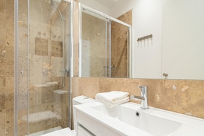Un baño moderno con cabina de ducha de vidrio, un lavabo blanco y un espejo grande.