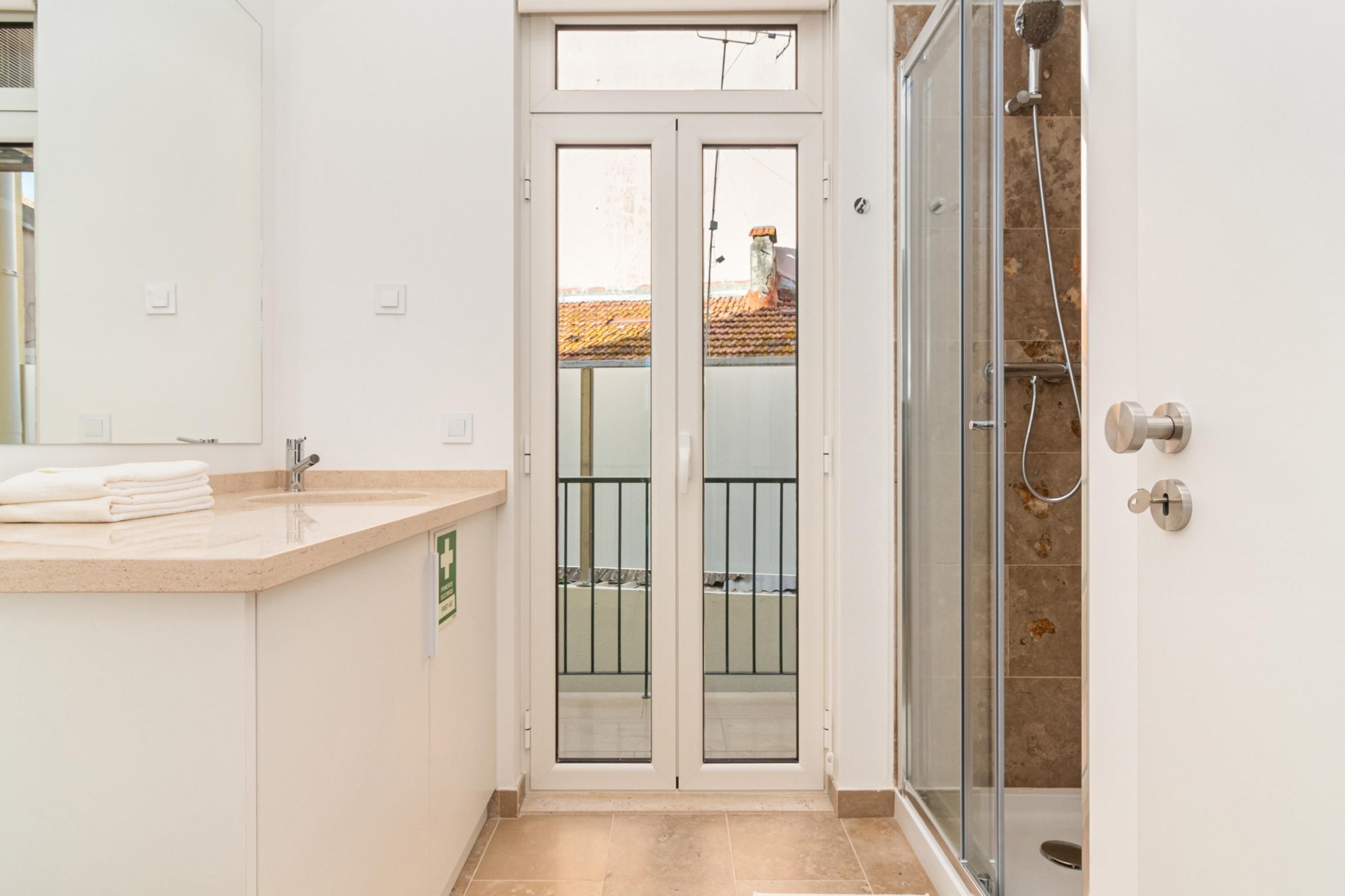 Un baño con ducha de vidrio, un lavamanos con encimera y una puerta que da a un balcón exterior.