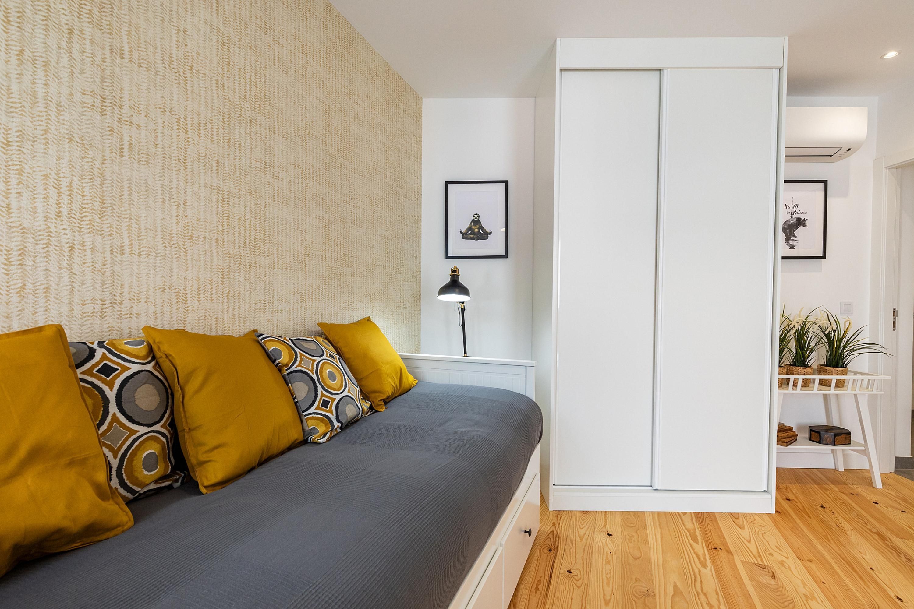 Una camera da letto moderna con un letto, cuscini a fantasia, un comodino con una lampada e un armadio.