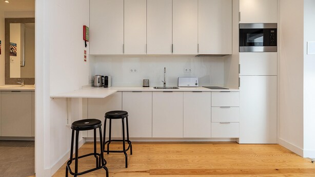 A modern kitchen with white cabinets, a microwave, a toaster, and two black stools. - Belem Design Studio 2 by Homing (Lisbon)