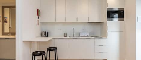 A modern kitchen with white cabinets, a microwave, a toaster, and two black stools.
