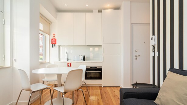 Un espacio habitable compacto con kitchenette, un comedor con mesa y sillas redondas, y un sofá con cojín.