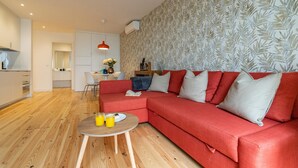 Ein modernes Wohnzimmer mit einem roten Ecksofa, einem runden Holztisch und einem Essbereich im Hintergrund.