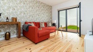 Ein modernes Wohnzimmer mit einem roten Sofa, Holzboden, einer Glastür, die auf einen Balkon führt, und einem Wandpapier mit Muster.