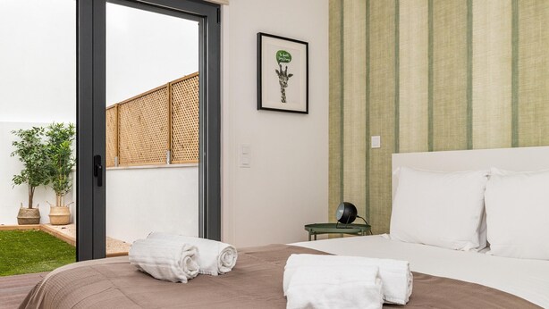 Ein Hotelzimmer mit einem Bett, zwei zusammengerollten Handtüchern, einem kleinen Tisch mit einer Uhr und einem gerahmten Bild an der Wand.
