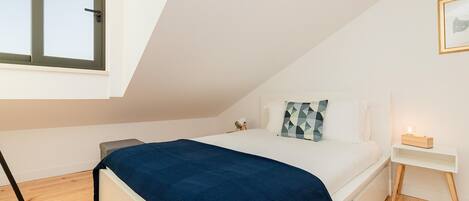 A bedroom with a bed, a bedside table, a nightstand, a window, and a picture on the wall.