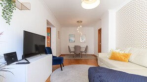 Un salon moderne avec un téléviseur à écran plat, un canapé, une table à manger avec des chaises et un escalier.