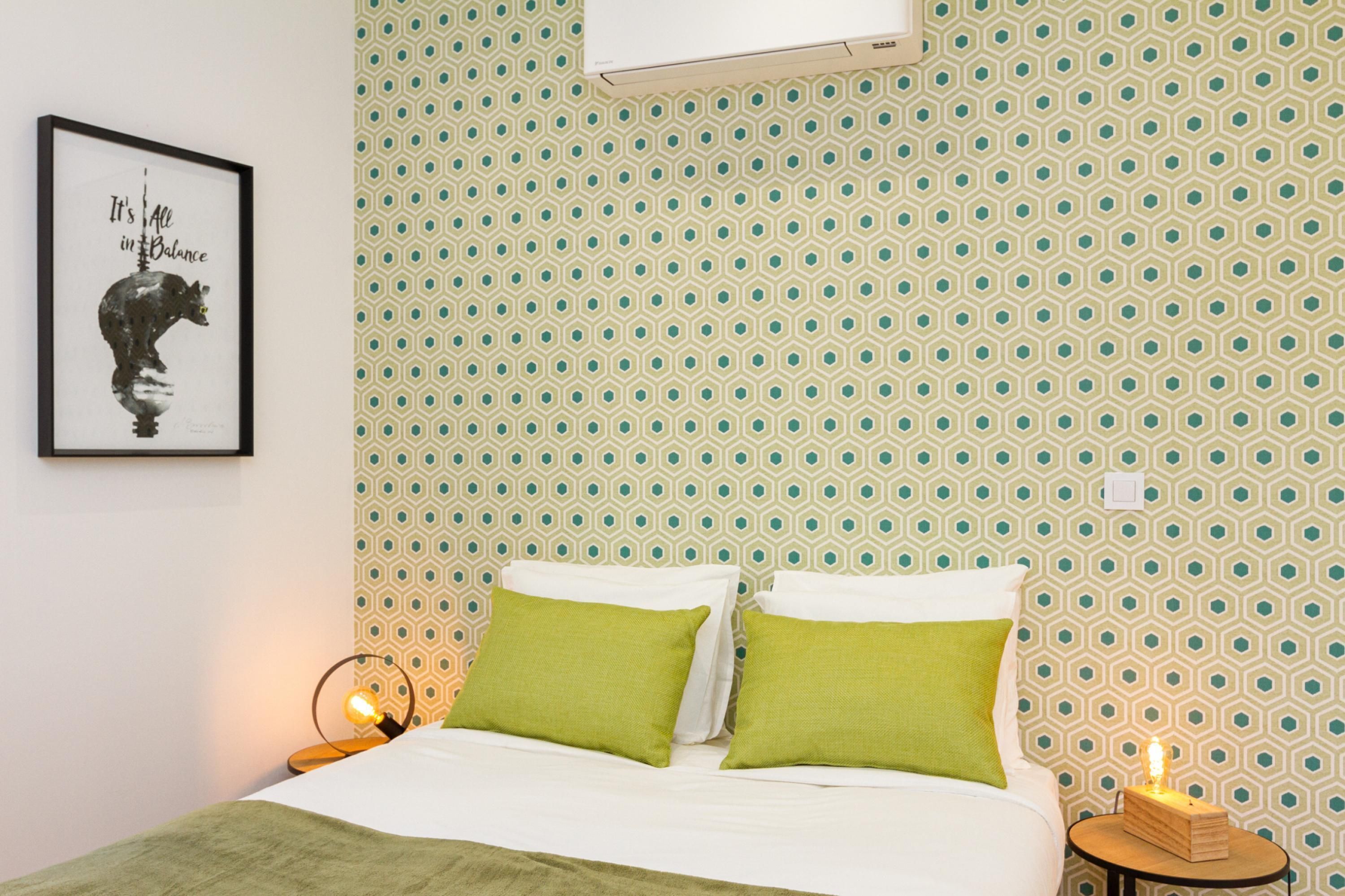 A bedroom with a patterned wallpaper, a framed quote on the wall, and a bedside lamp.