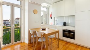 Une cuisine moderne avec des meubles blancs, une table à manger en bois et une vue dégagée grâce aux portes-fenêtres coulissantes.